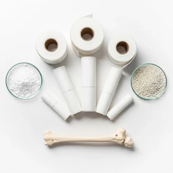 باند فایبرگلاس در کنار پودر هیدروکسی‌آپاتیت و دانه‌های شیشه زیست‌فعال روی پس‌زمینه سفید